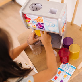 A kid playing with The Melissa & Doug Wooden Thirst Quencher Drink Dispenser With Cups, Juice Inserts, Ice Cubes